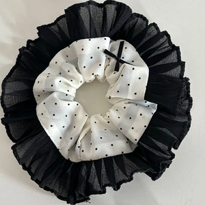 Close-up of black and white polka dot scrunchie with lace trim and small ribbon bow
