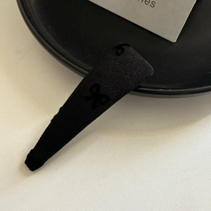 Dettaglio ravvicinato di un fermaglio per capelli BB in tessuto nero con un piccolo fiocco