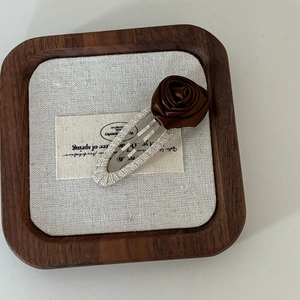 Close-up of a brown satin rose hair clip with silver glitter base on a wooden tray