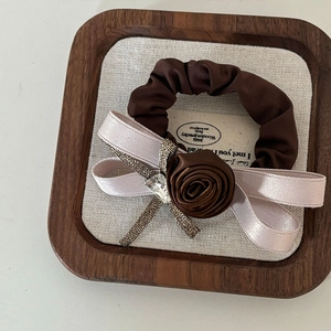 Macro detail of brown satin rose scrunchie with champagne ribbon and teardrop gem