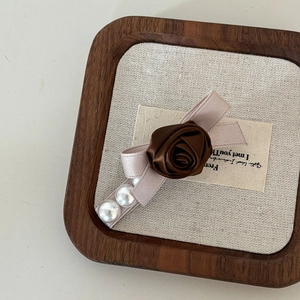 Detail of vintage brown rose hair clip with satin ribbon bow and pearl accents on tray