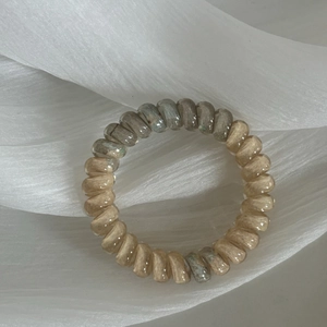 Detail of gradient spiral hair ties in champagne and green on soft silk fabric