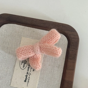 Pink knitted bow hair clip in soft yarn with a 3D woven texture on rustic tray