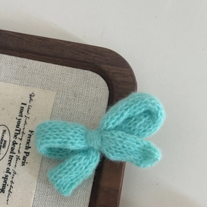 Handmade mint green knitted bow hair clip in a wooden tray with a cozy aesthetic vibe