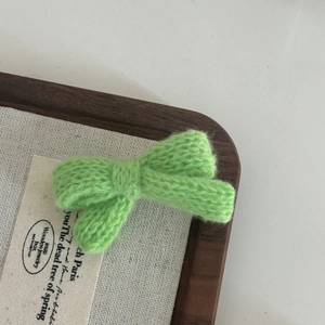 Close-up of grass green knitted bow hair clip with textured handmade woolen craftsmanship