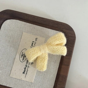 Macro shot of yellow knitted bow hair clip with textured weave on a wooden tray