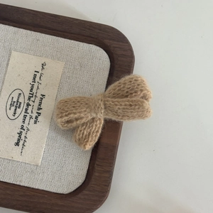 Detailed close-up of khaki crochet bow hair clip made with soft yarn on a wooden display base