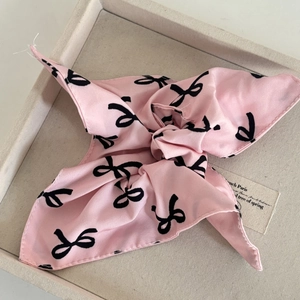 Detail view of pink satin scarf with black bow patterns showing the soft fabric texture