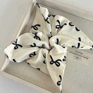 Elegant beige satin scrunchie with black bow print on a soft velvet jewelry tray