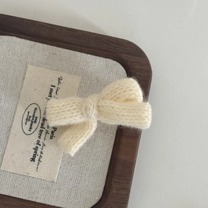 Close-up of cream knit bow hairpin showing detailed hand-woven texture on a wooden tray