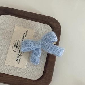 Detail of light blue knitted bow hair clip showing handmade yarn texture and metal base