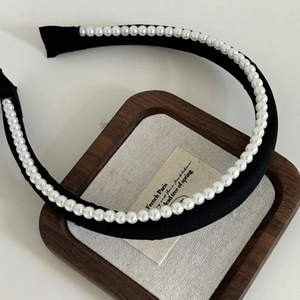 Close-up of black wide headband with a row of elegant white pearls on a display tray