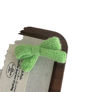Handmade light green knitted bow hair clip on a vintage wooden display box