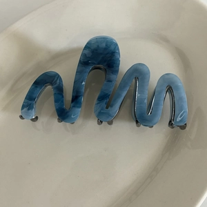 Detail of wave-shaped hair claw clip with blue marble pattern and metal teeth