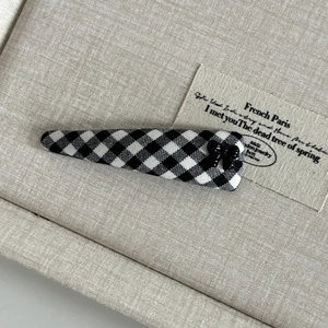 Detail of British style black and white checkered hair clip with small bow on linen base