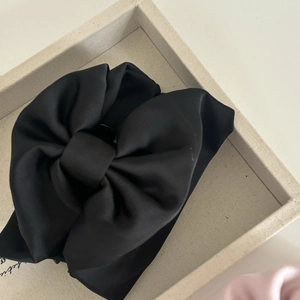 Close-up of elegant black satin bow hair claw clip showing silky fabric texture details