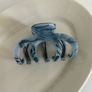 Macro detail of ink-wash gray marble acetate hair claw clip on ceramic tray