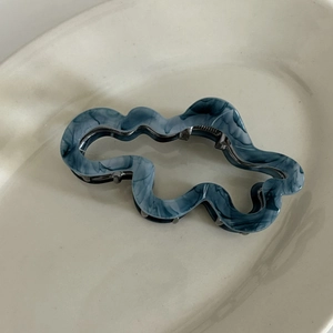 Detail showing marble grey acetate hair claw clip with irregular wave pattern on ceramic tray
