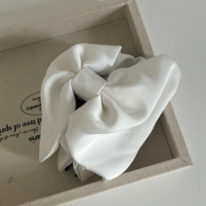 Close-up of a large white satin bow hair claw clip with elegant silky texture on a tray