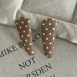 Close-up of brown teardrop hair clips with white polka dots on rustic linen fabric