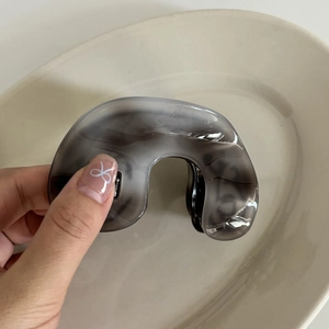 Detail of the grey marble pattern acetate hair claw clip held by hand over a white plate