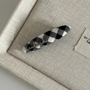 Close-up of gingham hair clip with silver handmade metal script on linen tray