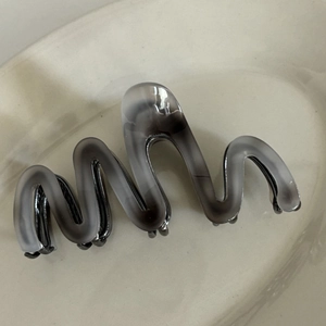 Detail of grey ink-wash marbled acetate hair claw clip with wavy edge on ceramic tray