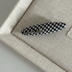 Macro detail of houndstooth fabric hair clip with a silver handmade metal charm