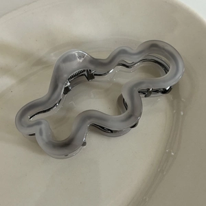 Detail view of wavy irregular grey acetate claw clip with frosted texture and silver spring