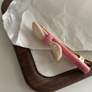 Dettaglio del fermaglio per capelli a fiocco in acetato rosa e beige su vassoio di legno