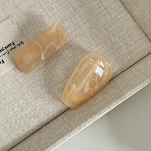 Détail de deux barrettes en acrylique ambré avec motifs marbrés sur tissu beige