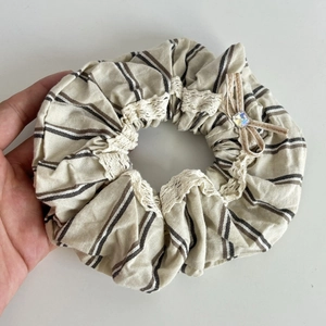 Macro shot of striped fabric scrunchie with white lace trim and rhinestone bow detail
