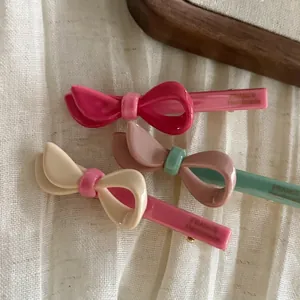 Tre fermagli per capelli a fiocco in acetato in colori a contrasto su sfondo in tessuto