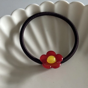 Detail eines hochelastischen schwarzen Haargummis mit roter Blume in Schale
