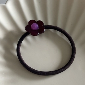 Detailansicht eines elastischen Haargummis mit glänzender lila Harzblume und Perle