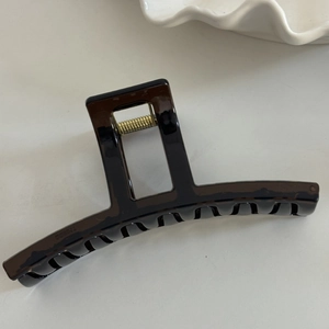 Close-up of a large amber translucent hair claw clip on a minimalist white table