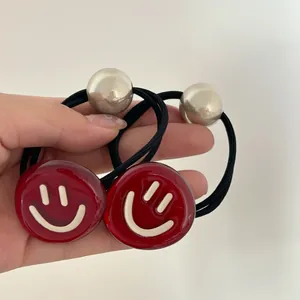 Détail du pendentif smiley rouge et de la perle argentée sur un élastique à cheveux noir