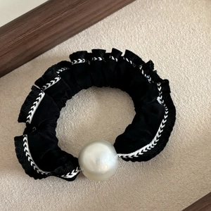 Detail of vintage black satin scrunchie with white stitching and large pearl accent