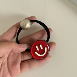 Détail de l'élastique à cheveux en acétate rouge avec visage souriant et perle argentée
