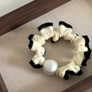 Detail view of large cream scrunchie with black ruffled edges and a decorative pearl bead