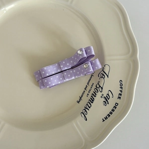 Vintage purple polka dot bow hair clips with central rhinestone on a ceramic plate