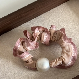 Pink and beige ruffled scrunchie with large pearl accent on a textured background