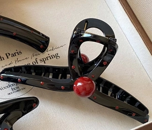 Close-up of elegant black hair claw clips with red pearls in a wooden jewelry box display