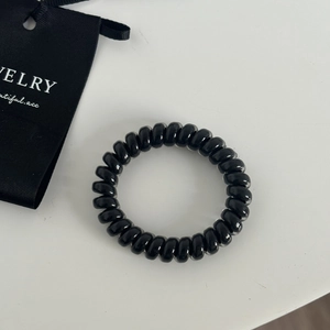 Close-up of a black spiral hair tie on white surface with a jewelry bag