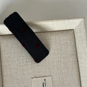 Sweet navy blue fabric hair clip with red heart pattern on beige tray background
