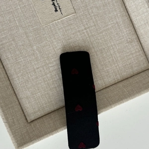 Rectangle black fabric hair clip with red heart patterns on a beige display tray