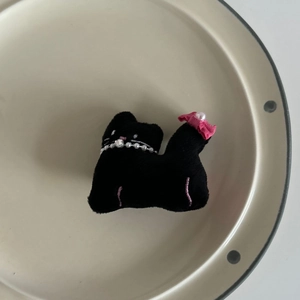 Detailed view of plush black cat hair clip with pink bow and pearl necklace charm