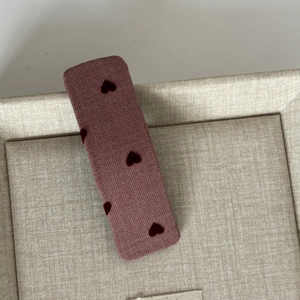 Sweet red fabric hair clip with flocked heart patterns on a beige display tray