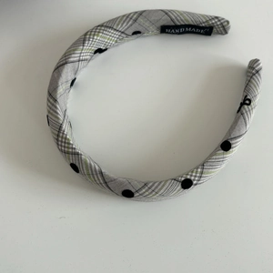 Detail of grey plaid headband with black dots and a white Hand Made label on the inner side