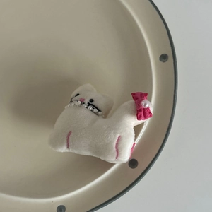 Close-up of cute white plush cat hair clip with pink bow and pearl on a ceramic plate
